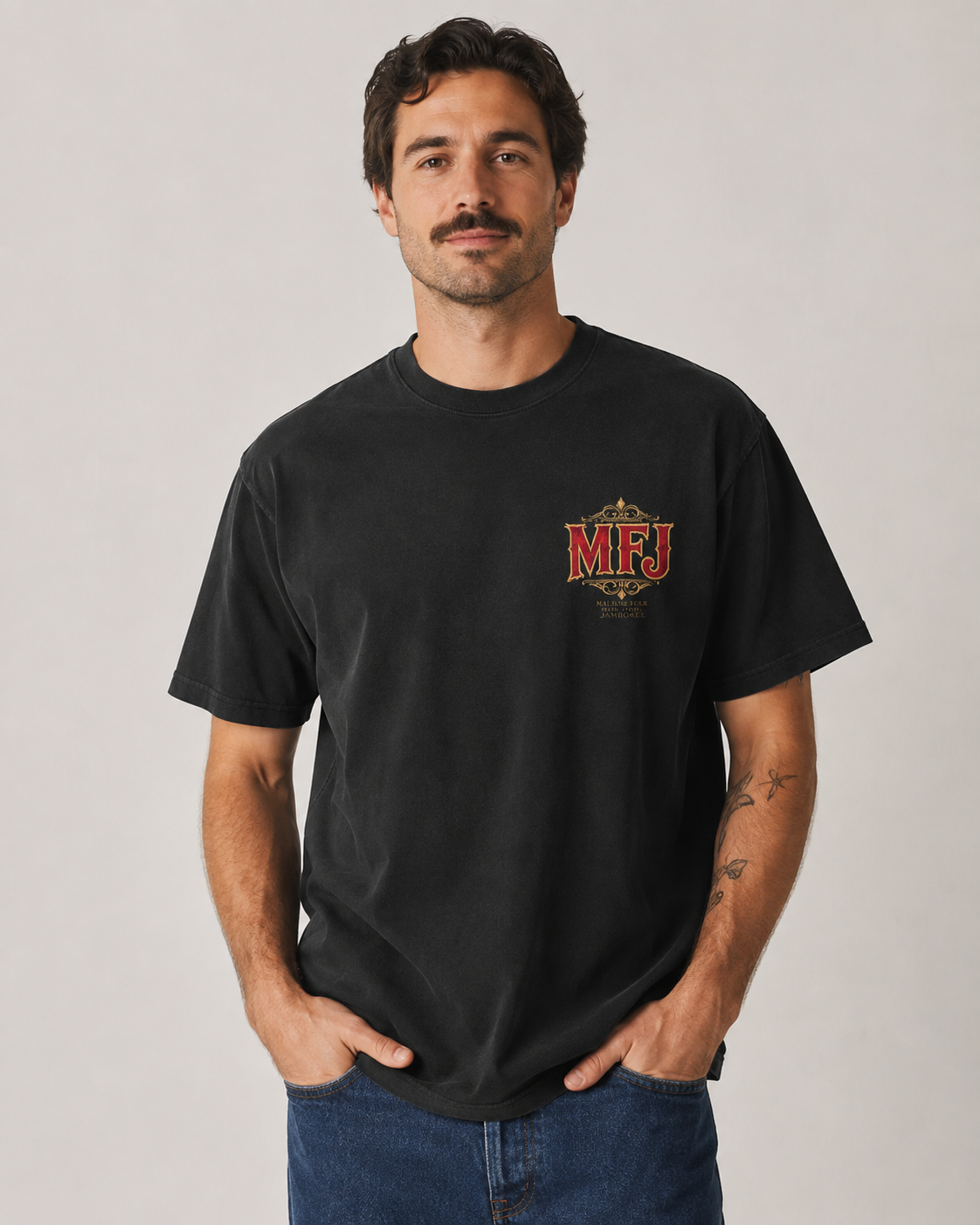 Male model wearing a black MFJ Theatre Critics heavyweight garment-dyed tee, showing the small MFJ left-chest graphic